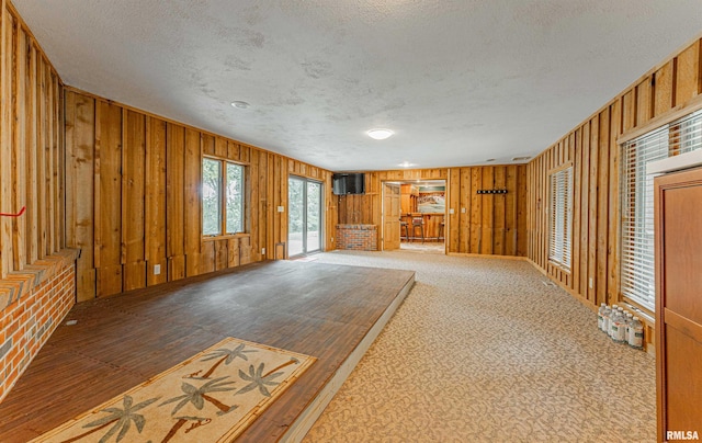 unfurnished living room with wooden walls, a textured ceiling, and carpet floors