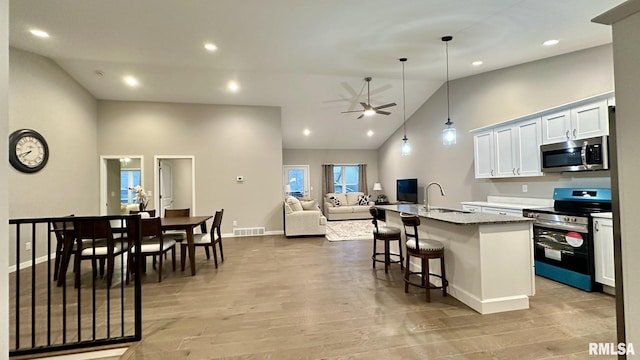 kitchen with white cabinets, a center island with sink, sink, appliances with stainless steel finishes, and decorative light fixtures