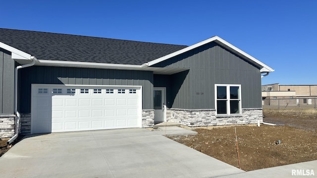 view of front of property featuring driveway, a garage, stone siding, roof with shingles, and fence