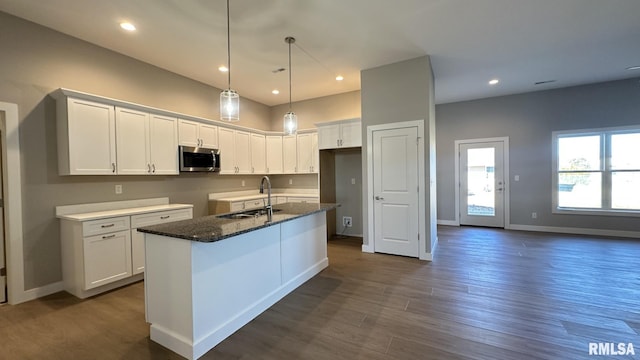 kitchen with a center island with sink, white cabinets, stainless steel microwave, dark wood-style flooring, and a sink