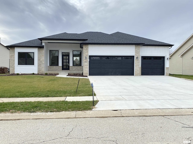 view of front facade with driveway, a shingled roof, stone siding, an attached garage, and a front lawn