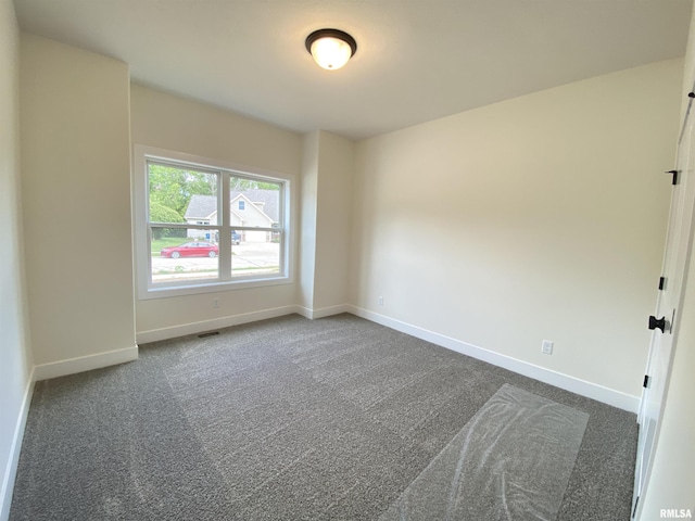 unfurnished room with visible vents, dark carpet, and baseboards