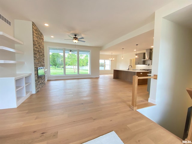 unfurnished living room featuring a fireplace, light hardwood / wood-style flooring, ceiling fan with notable chandelier, and sink