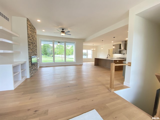 unfurnished living room with light wood finished floors, recessed lighting, visible vents, a stone fireplace, and ceiling fan with notable chandelier