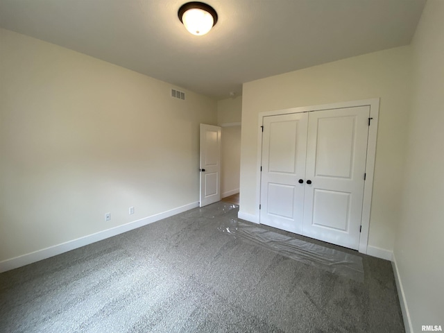 unfurnished bedroom with a closet, visible vents, dark carpet, and baseboards