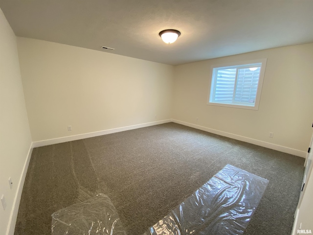 empty room featuring visible vents, dark carpet, and baseboards