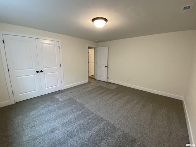 unfurnished bedroom with visible vents, baseboards, dark colored carpet, and a closet