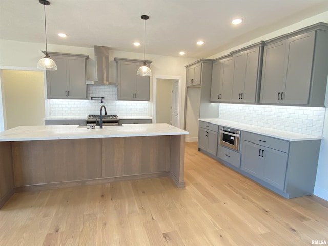 kitchen with light wood-type flooring, gray cabinets, wall chimney exhaust hood, and light stone countertops