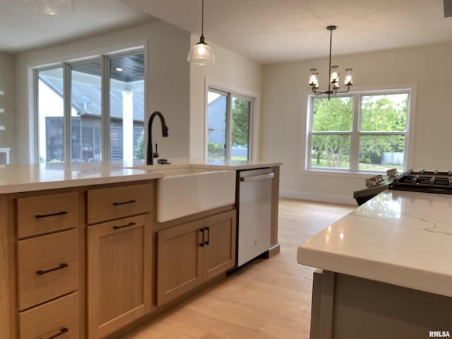 kitchen with a sink, light wood-style floors, stainless steel dishwasher, and hanging light fixtures