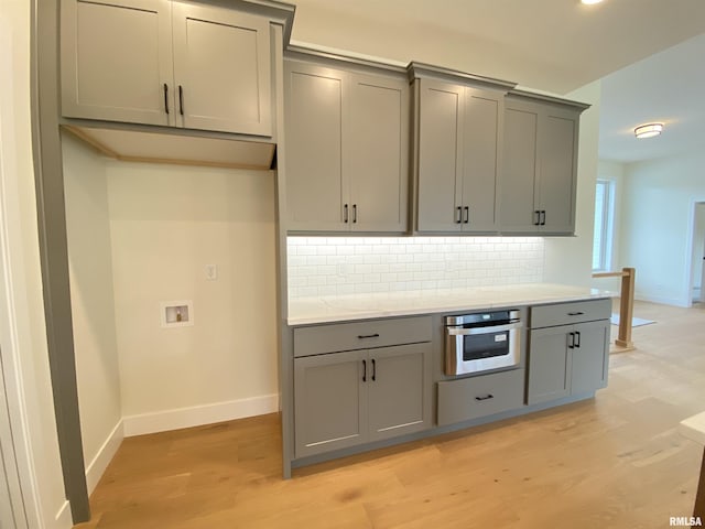 kitchen featuring light wood-style floors, gray cabinets, oven, and decorative backsplash