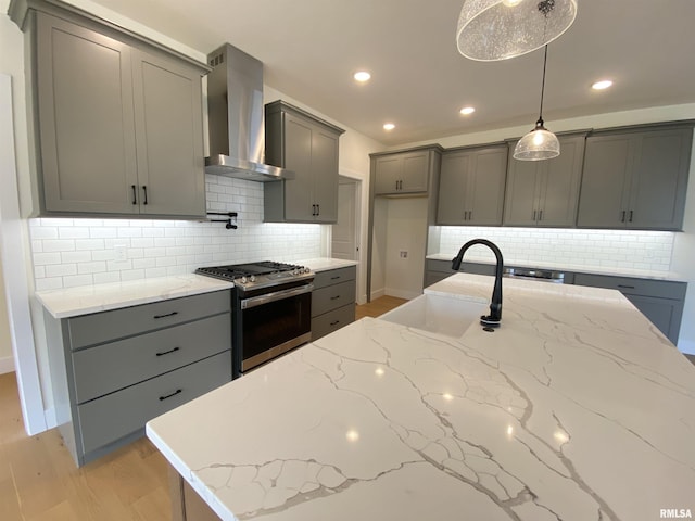 kitchen featuring wall chimney range hood, gray cabinetry, a sink, and gas range