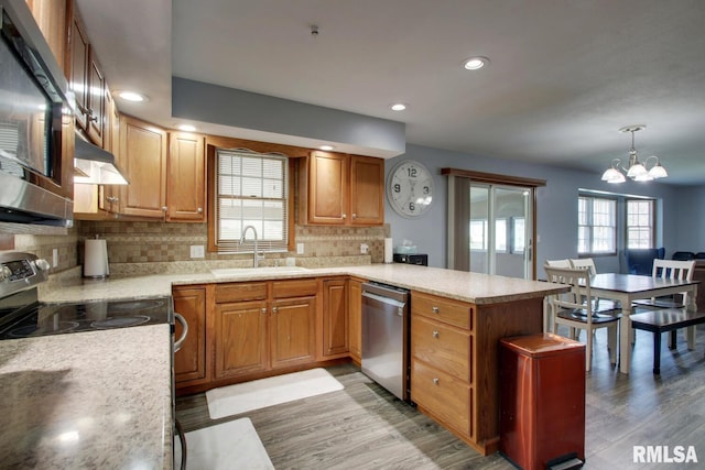 kitchen with hanging light fixtures, backsplash, an inviting chandelier, light hardwood / wood-style flooring, and stainless steel appliances