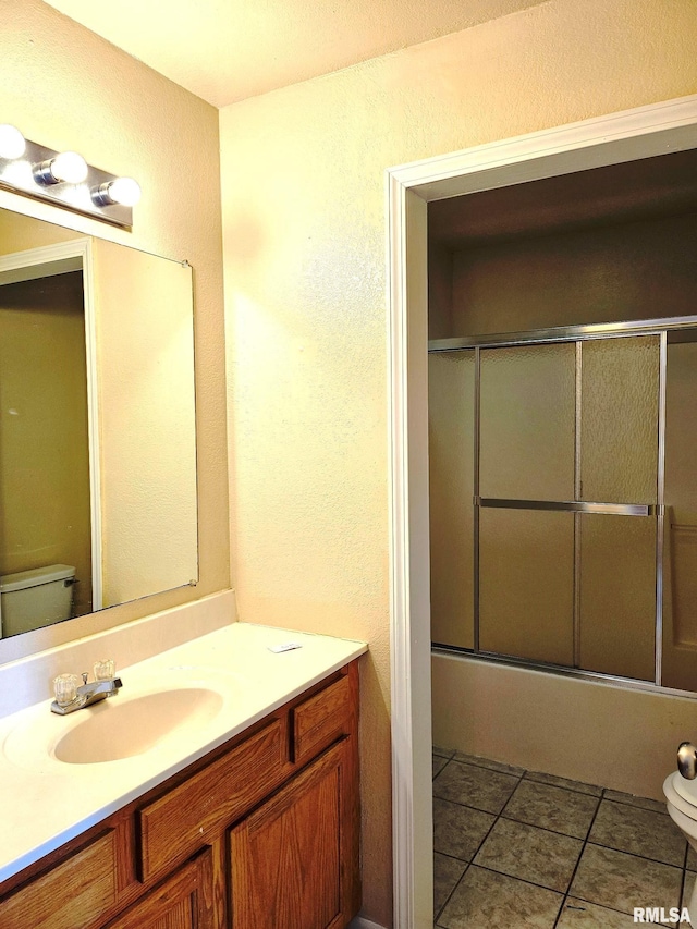 full bathroom with tile patterned flooring, bath / shower combo with glass door, vanity, and toilet