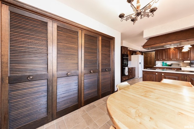 kitchen with white refrigerator with ice dispenser, an inviting chandelier, double wall oven, dark brown cabinets, and decorative light fixtures