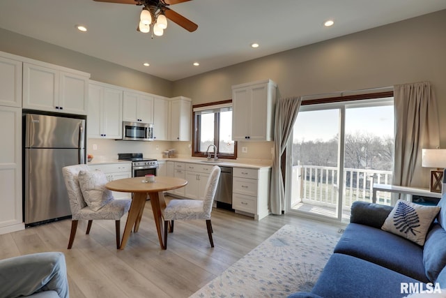 kitchen with light hardwood / wood-style floors, sink, white cabinets, stainless steel appliances, and ceiling fan