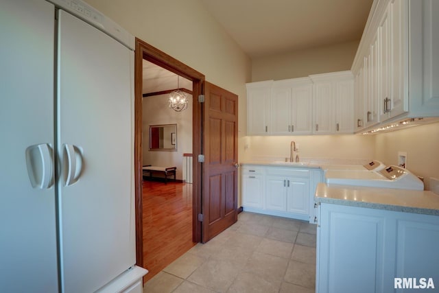 clothes washing area with cabinets, light hardwood / wood-style floors, washer and dryer, sink, and a notable chandelier