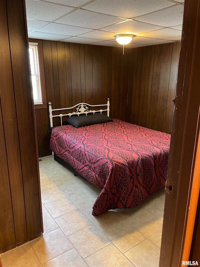 bedroom featuring wooden walls, light tile floors, and a drop ceiling