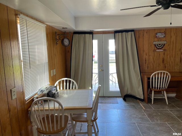 dining space with french doors, wooden walls, dark tile floors, and ceiling fan