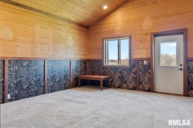 carpeted empty room with wood ceiling, wooden walls, high vaulted ceiling, and a wealth of natural light