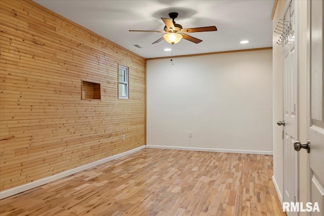 spare room featuring ornamental molding, ceiling fan, light hardwood / wood-style flooring, and wooden walls