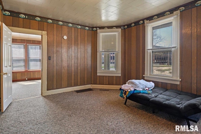 unfurnished room with carpet flooring, plenty of natural light, and wood walls