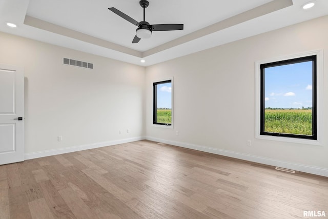 spare room with ceiling fan, a raised ceiling, and light wood-type flooring