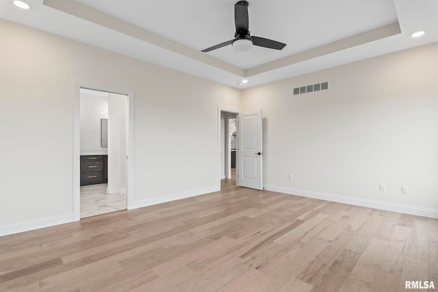 unfurnished bedroom with light hardwood / wood-style flooring, connected bathroom, a tray ceiling, and ceiling fan