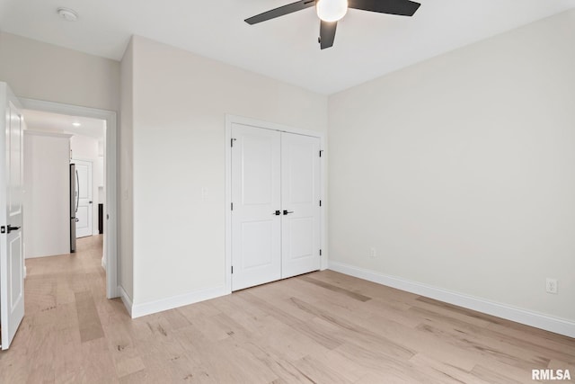 unfurnished bedroom featuring stainless steel refrigerator, ceiling fan, light hardwood / wood-style flooring, and a closet