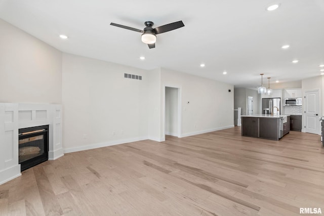 unfurnished living room with light wood-type flooring, ceiling fan, and sink