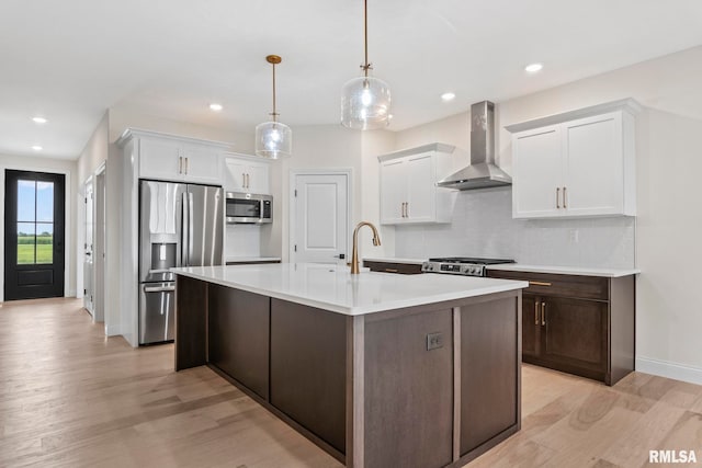 kitchen with wall chimney exhaust hood, light wood-type flooring, white cabinetry, and appliances with stainless steel finishes