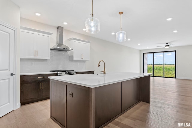 kitchen with white cabinetry, wall chimney exhaust hood, light wood-type flooring, stainless steel range oven, and decorative light fixtures