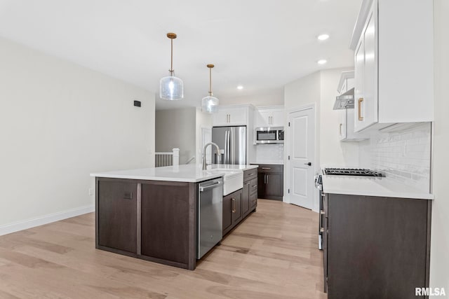 kitchen with appliances with stainless steel finishes, light hardwood / wood-style floors, white cabinets, dark brown cabinetry, and a kitchen island with sink