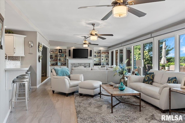 living room featuring built in shelves, light wood-type flooring, and ceiling fan