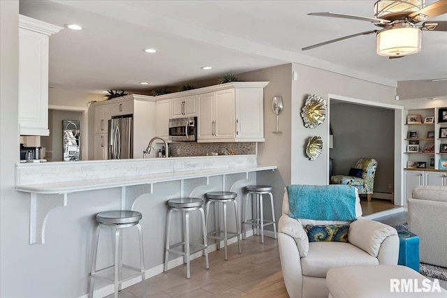 kitchen featuring white cabinets, a kitchen breakfast bar, appliances with stainless steel finishes, light hardwood / wood-style floors, and kitchen peninsula