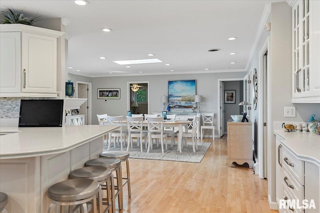 kitchen with tasteful backsplash, a breakfast bar, crown molding, light hardwood / wood-style flooring, and white cabinetry