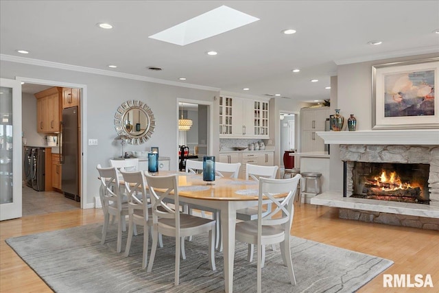 dining area with light hardwood / wood-style floors, a stone fireplace, ornamental molding, and a skylight