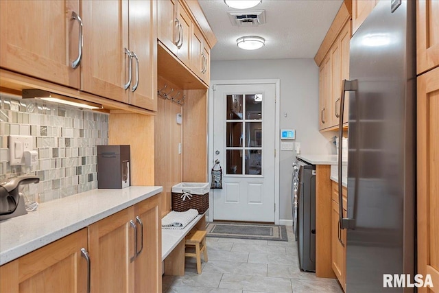 kitchen with decorative backsplash, washer and dryer, light tile patterned floors, light stone counters, and stainless steel refrigerator