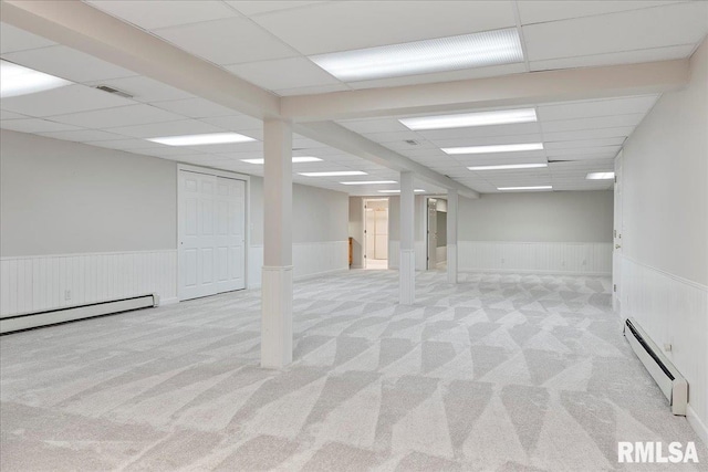 basement featuring a drop ceiling, light colored carpet, and baseboard heating