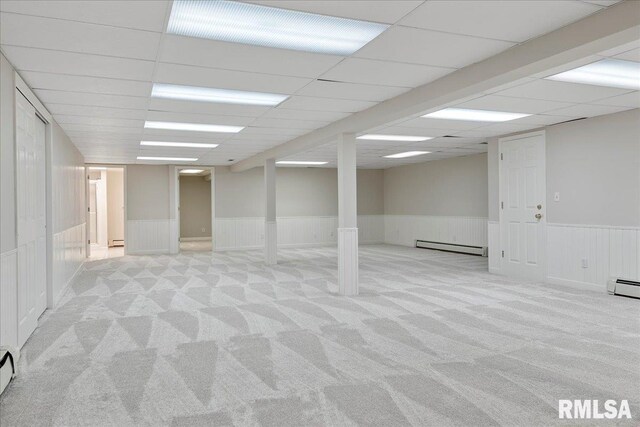 basement featuring a paneled ceiling, baseboard heating, and light carpet