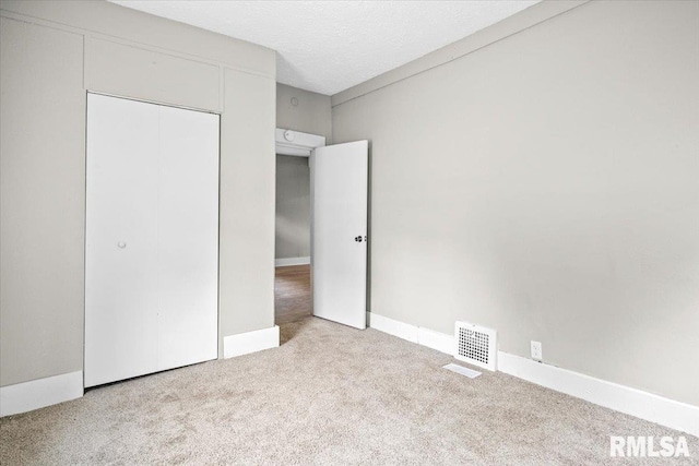 unfurnished bedroom featuring a textured ceiling, light carpet, and a closet