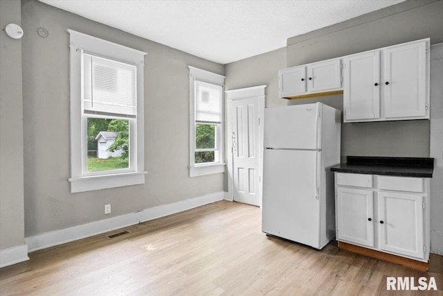 kitchen with white cabinets, light hardwood / wood-style flooring, white fridge, and a textured ceiling