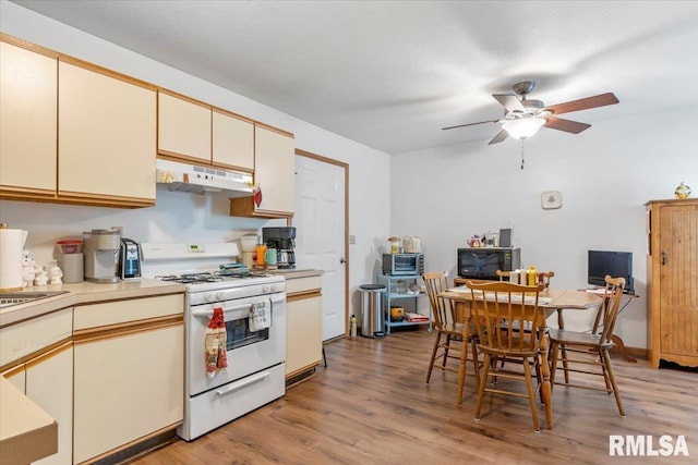 kitchen featuring ceiling fan, white range with gas stovetop, a textured ceiling, cream cabinetry, and light wood-type flooring