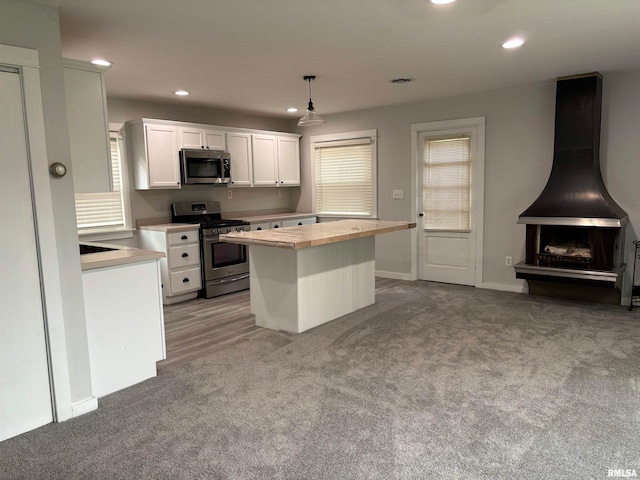 kitchen with white cabinets, stainless steel appliances, a center island, decorative light fixtures, and light carpet