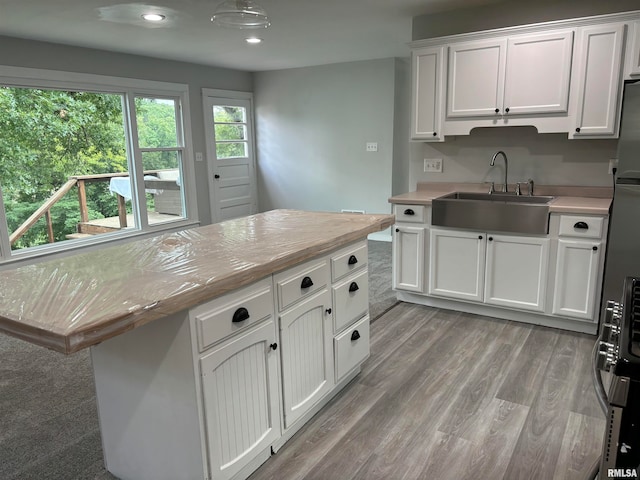 kitchen with light wood-type flooring, a center island, sink, and white cabinets