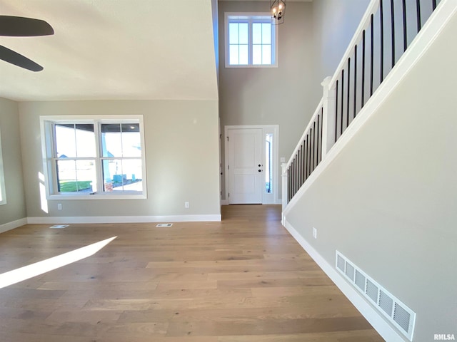 foyer entrance with hardwood / wood-style floors, a towering ceiling, and ceiling fan with notable chandelier