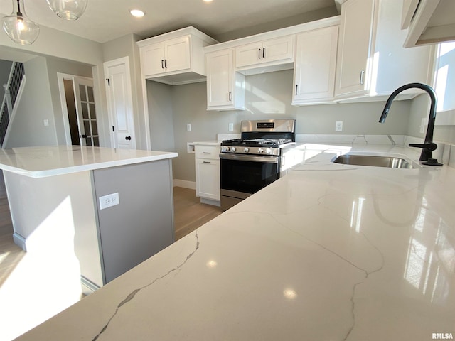 kitchen featuring pendant lighting, light stone counters, white cabinetry, and stainless steel gas range