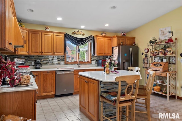 kitchen with sink, appliances with stainless steel finishes, light tile patterned floors, a kitchen island, and decorative backsplash