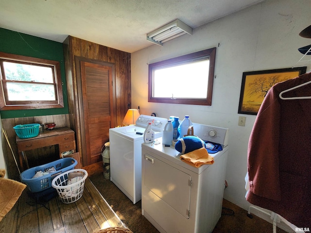 washroom featuring washing machine and dryer, a healthy amount of sunlight, and wood walls