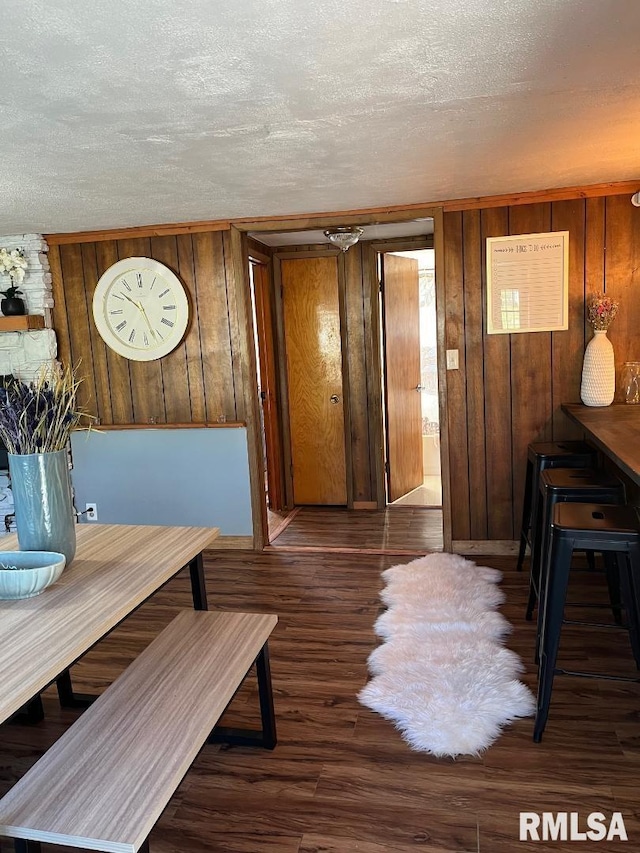 dining area with dark wood-type flooring, wood walls, and a textured ceiling