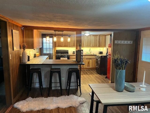 kitchen with black gas stove, pendant lighting, light wood-type flooring, a kitchen bar, and kitchen peninsula